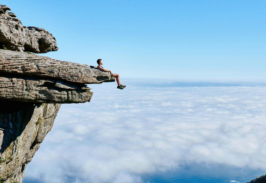 El Síntoma como un Mensaje del Cuerpo A person sits on a cliff edge enjoying a breathtaking view of the ocean and city below.